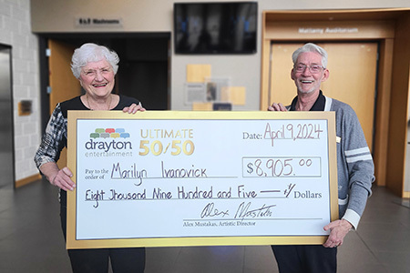 Marilyn Ivanovick and Gary Good hold a mock-up cheque in the foyer of Hamilton Family Theatre Cambridge