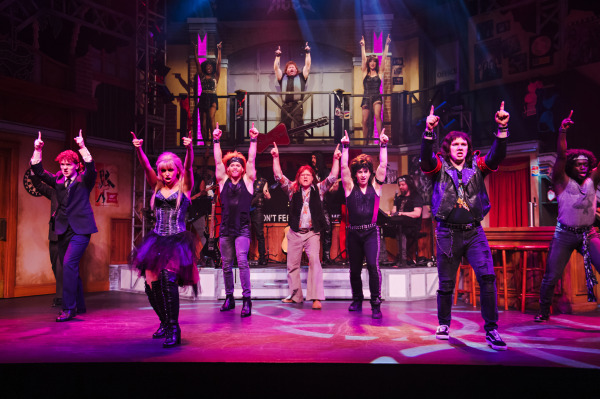 Production photo of Rock of Ages, showing the entire company dancing on stage with dramatic lighting.